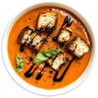 An image of a bowl of creamy tomato basil soup, topped with grilled cheese croutons and a drizzle of balsamic glaze. The creamy tomato basil soup, with its rich tomato flavor and aromatic basil, photo