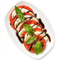 A classic Caprese salad with alternating slices of ripe tomatoes and fresh mozzarella, drizzled with balsamic glaze and olive oil. Fresh basil leaves add a pop of color and flavor, creating a simple photo