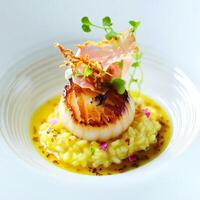 A tasting menu course featuring a seared scallop, served on a bed of saffron risotto, drizzled with truffle oil, and garnished with crispy prosciutto and shaved parmesan, presented in a small, elegant photo