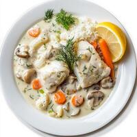 A plate of blanquette de poisson, a creamy fish stew, made with white fish fillets, mushrooms, carrots, pearl onions, and leeks, simmered in a white sauce with cream and lemon juice, resulting in a photo