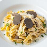 A plate of tagliatelle al tartufo estivo, featuring long, flat egg noodles, tossed in a creamy sauce, made with butter, parmesan cheese, and shaved summer truffles, resulting in a lighter yet photo