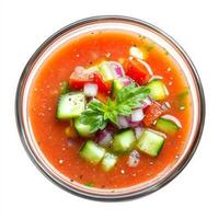 A vibrant summer gazpacho, a cold tomato-based soup blended with cucumbers, bell peppers, and onions, served in a glass bowl with a drizzle of olive oil. A refreshing and healthy dish. Isolated on photo