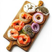 A wooden cutting board with an assortment of freshly baked bagels, served with cream cheese, smoked salmon, capers, and thinly sliced red onions. A classic breakfast option. Isolated on clean white photo