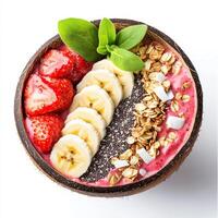 A vibrant smoothie bowl topped with sliced bananas, strawberries, shredded coconut, chia seeds, and granola, served in a coconut shell. A tropical and nutritious breakfast. Isolated on clean white photo