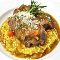 A plate of braised veal shank with saffron risotto alla Milanese, featuring tender veal shanks, braised slowly in a white wine sauce with vegetables, herbs, and a hint of saffron, served over a bed of photo