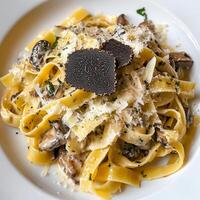 A plate of tagliatelle ai funghi porcini e tartufo, featuring long, flat egg noodles tossed in a rich and creamy sauce made with both porcini mushrooms and truffles, garlic, butter, cream, and photo