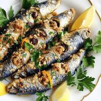 A plate of sarde a beccafico, featuring fresh sardines, stuffed with a flavorful mixture of breadcrumbs, pine nuts, currants, parsley, and orange zest, rolled up and baked with bay leaves and white photo