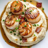 A plate of seared scallops with cauliflower puree, featuring tender seared scallops served over a smooth and creamy cauliflower puree, drizzled with a brown butter sauce and garnished with crispy photo