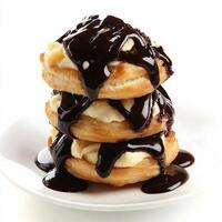 A close-up of a profiterole au chocolat, a cream puff filled with vanilla pastry cream and topped with chocolate sauce, arranged in a stack on a plate, showcasing the light and airy pastry and the rich chocolate, isolated on clean white background. photo