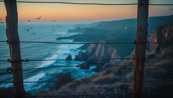 Ocean View From Cliffside with Wooden Fence and Flying Birds at Sunset photo