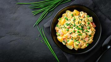 Bowl of potato salad with peas and chives on black table setting, ready for lunch photo