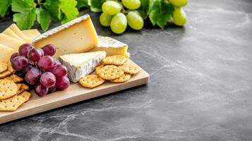 Cheese, crackers, and grapes are arranged for snacking on a marble table, with leaves around photo