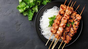 Grilled meat skewers with rice noodles, parsley on dark surface, can be used in food blog photo
