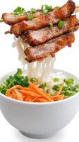 Grilled pork skewers over noodles, carrots, and greens in a white bowl on a white background photo