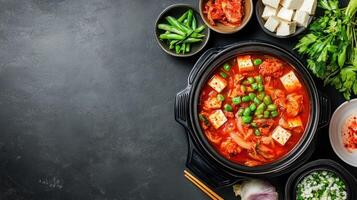 Korean spicy soup with tofu and vegetables ready for serving at rustic dark textured table photo