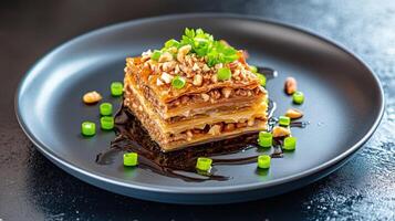 Layered dessert on plate. Nuts, parsley, and green onion topping. Dark background with some sauce. Possible gourmet use photo
