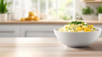 Mashed potatoes in bowl with chives and cheese on table in kitchen, background is blurred photo