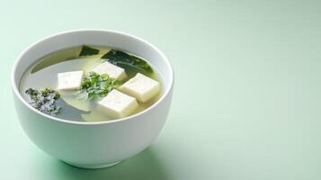 Miso soup in bowl with tofu and seaweed on pastel surface for health and diet photo