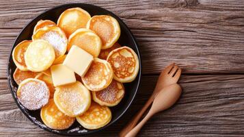 Mini pancakes with butter on a plate with cutlery and wooden background. Use for recipes, blogs photo