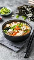 Miso soup with tofu and seaweed with chives background in a bowl on the stone table for commercial use photo