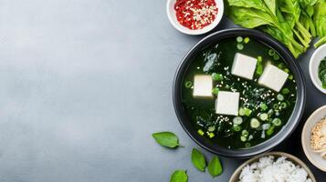 Miso soup with tofu in bowl, with rice and spinach around on the grey surface, for wellness photo