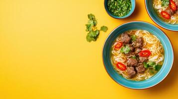 Noodles in broth with meat and pepper, with garnish and sauce on yellow backdrop. Food blog photo