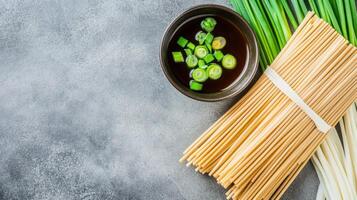 Noodles ready to cook, with broth and green onion, on grey textured table, for a food blog post photo