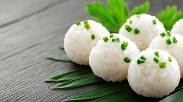 Rice balls with green garnish on leaves, resting on a gray wood surface. Food photography photo