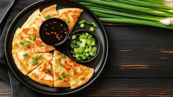 Scallion pancake wedges on a dark plate, with dark dipping sauce and onions in the background, for food blog photo