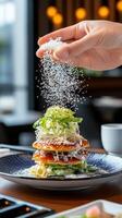 Sprinkling salt on a fancy, layered salad in a cafe blurred background, could be used for food blog photo