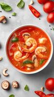 Tom Yum soup with shrimp, mushrooms, and tomatoes on a light gray background. Use for food blog photo