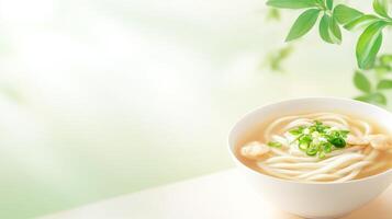 Udon noodle soup in bowl, garnished with scallions, on tabletop. Green foliage background. Stock image for food blog photo