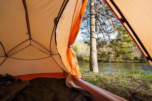Enjoy a Cozy Campsite View Experience the tranquility of relaxing inside a warm tent positioned right beside a serene river, surrounded by beautiful scenery and abundant greenery all around photo