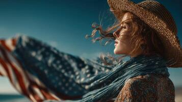 Woman in straw hat stands on the beach with wind-blown scarf and a flag draped behind her during a bright day photo