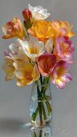 Beautiful bouquet of colorful freesias in a glass vase with water on a light background photo