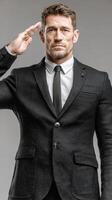Suit-clad man saluting with confidence in a neutral backdrop, showcasing professionalism and respect photo