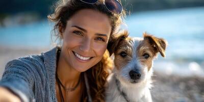 Woman smiles with her dog on a beach during a sunny day, capturing a joyful moment together by the water photo