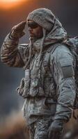 Soldier salutes at sunset in cold terrain, clad in tactical gear and winter clothing photo