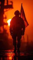 Soldier stands against sunset backdrop holding American flag in dramatic silhouette photo