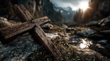 Wooden cross rests on rocky ground near a stream at sunset in a serene mountainous landscape photo