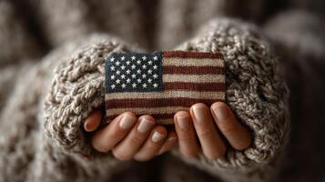 Hands hold small fabric patch with American flag design, cozy atmosphere and textured sweater in background photo