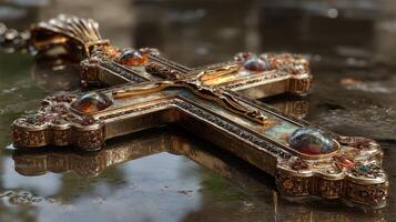 Intricate cross pendant resting on a wet surface reflecting its ornate design during late afternoon photo