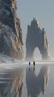 Two hikers explore a snowy coastline under a towering rock formation in winter light photo