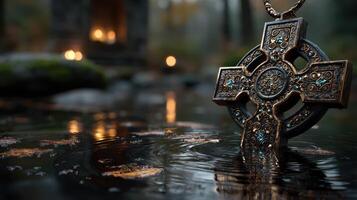 Celtic cross pendant resting on water with reflections during early evening in a lush forest setting photo