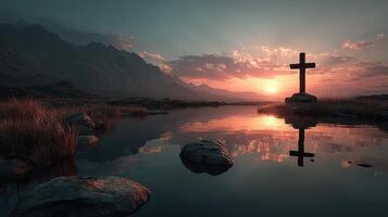Serene sunset over a reflective lake with a cross in the foreground and mountains in the background photo