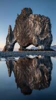 Rocky formation at Hvitserkur beach reflects in tranquil water during sunset, creating a breathtaking natural spectacle photo