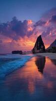Vibrant sunset reflects on tranquil beach with rocky formations in the background photo