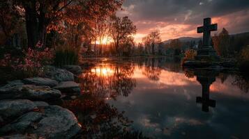 Beautiful autumn sunset reflecting on still water beside a cemetery with a cross and colorful foliage photo