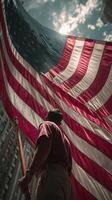 Person displaying large American flag against bright sky in urban setting during daytime photo