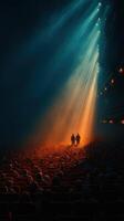 Crowd gathers in a theater as two figures walk toward vibrant light during a performance photo